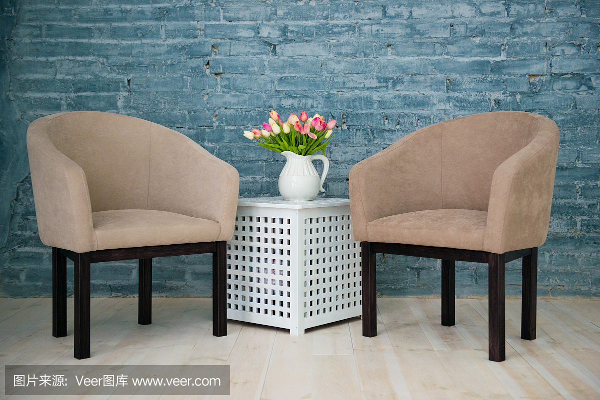兩張灰色扶手椅、一張桌子和靠在灰色磚墻邊的花。室內(nèi)